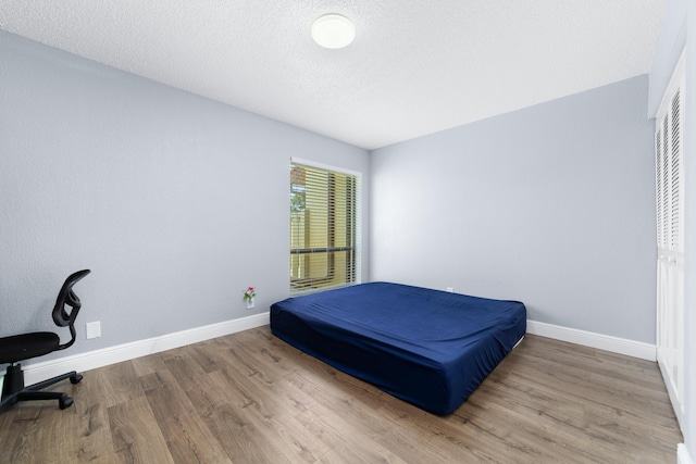 bedroom featuring baseboards, wood finished floors, and a textured ceiling