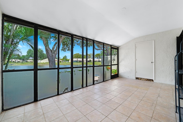empty room featuring expansive windows, vaulted ceiling, a textured wall, light tile patterned floors, and a water view