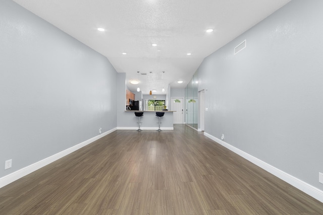 unfurnished living room with visible vents, baseboards, a textured ceiling, and dark wood-style floors