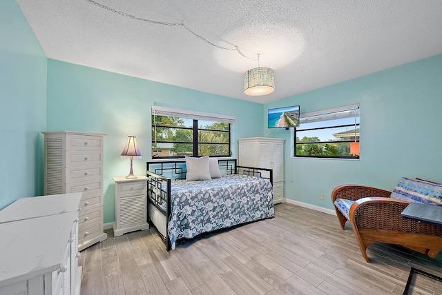 bedroom featuring light wood-type flooring, baseboards, multiple windows, and a textured ceiling