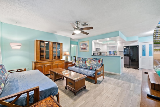 living area featuring visible vents, a textured ceiling, light wood-type flooring, and a ceiling fan