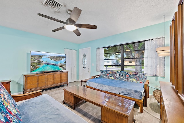 bedroom with light wood-style flooring, a textured ceiling, ceiling fan, and visible vents