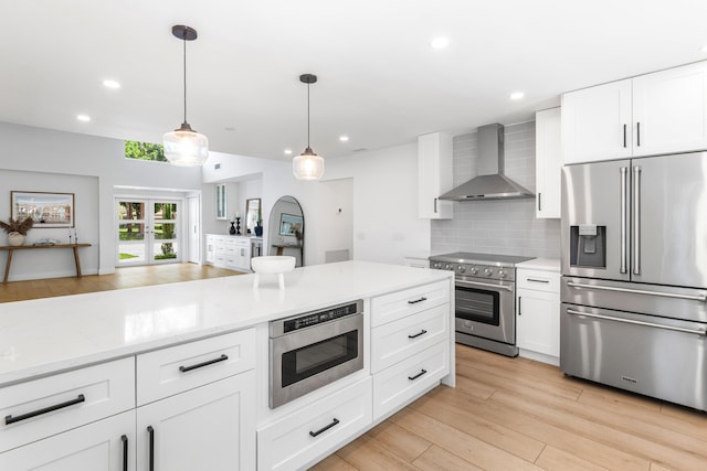 654 Lakewoode Cir W, Delray Beach, FL 33445 - kitchen with high quality appliances, wall chimney range hood, decorative backsplash, light wood-style floors, and pendant lighting