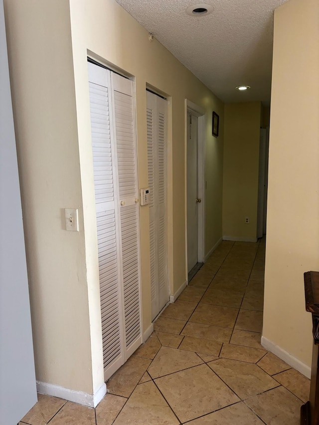 hall with light tile patterned floors, a textured ceiling, and baseboards