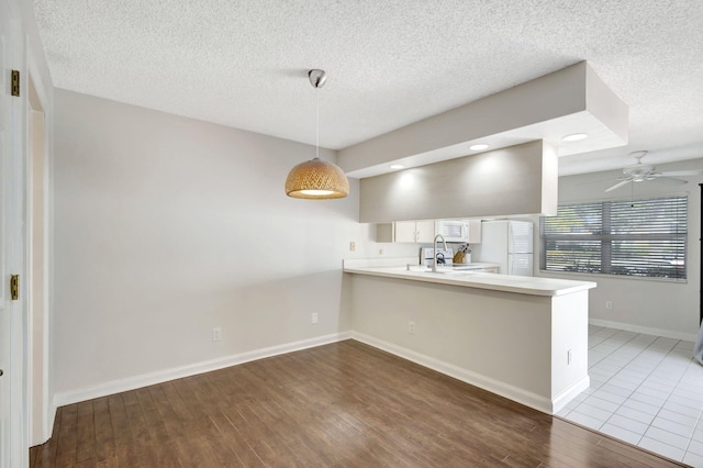 kitchen with white appliances, a peninsula, a ceiling fan, wood finished floors, and light countertops