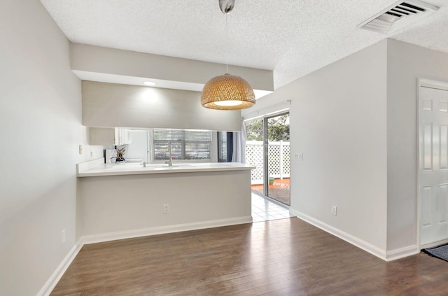 kitchen featuring baseboards, a peninsula, a textured ceiling, visible vents, and wood finished floors