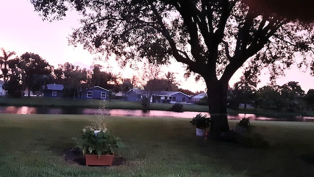 yard at dusk featuring a water view and a lawn