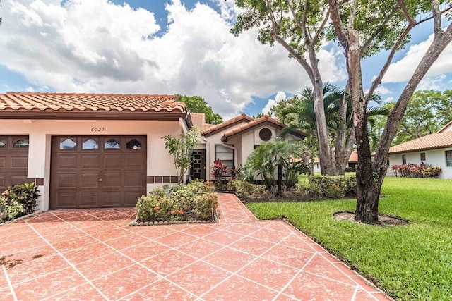 mediterranean / spanish house featuring a tiled roof, stucco siding, a front lawn, an attached garage, and driveway