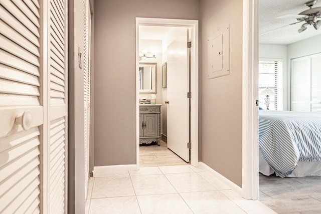 hallway featuring a textured ceiling, light tile patterned flooring, baseboards, and electric panel