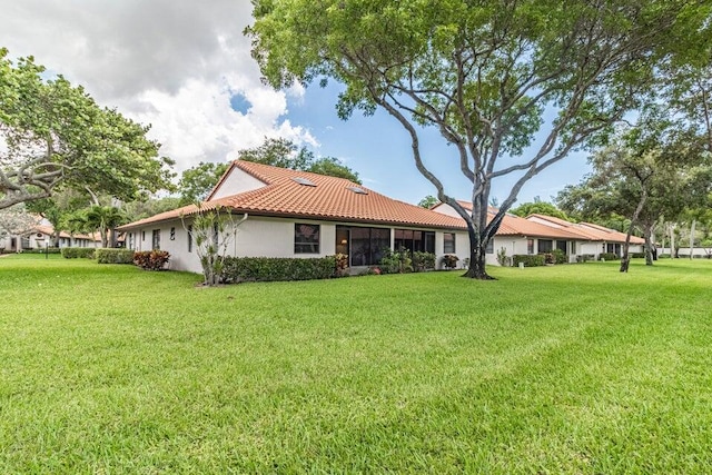 rear view of house featuring a tiled roof, stucco siding, and a lawn