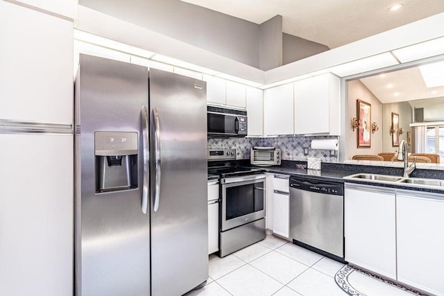 kitchen featuring a sink, dark countertops, white cabinetry, vaulted ceiling, and stainless steel appliances