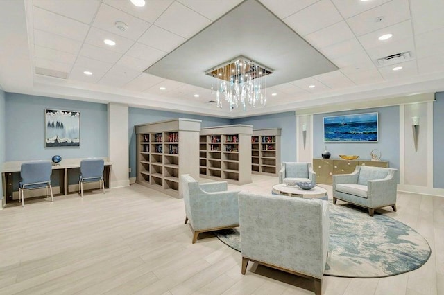 living area featuring visible vents, baseboards, a raised ceiling, an inviting chandelier, and wood finished floors