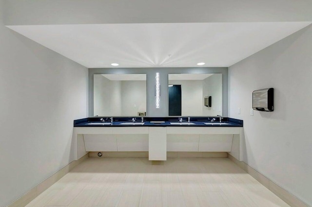 full bath featuring double vanity, a sink, and baseboards