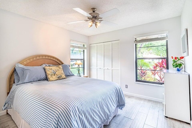 bedroom featuring a closet, light wood-type flooring, baseboards, and a textured ceiling