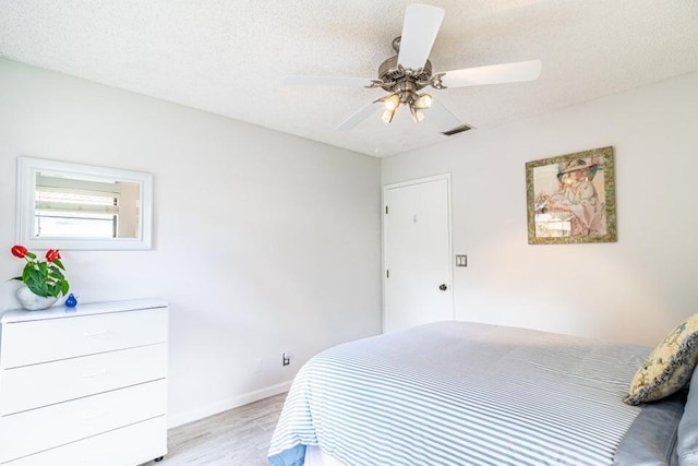 bedroom with ceiling fan, light wood-style flooring, a textured ceiling, visible vents, and baseboards