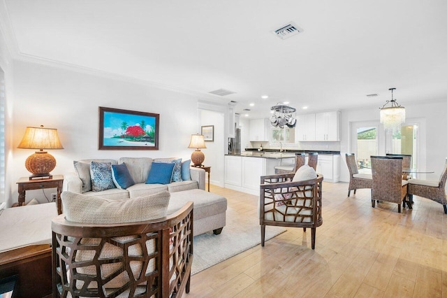 living room with light wood finished floors, a notable chandelier, visible vents, and ornamental molding