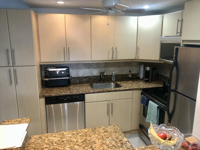 kitchen featuring a ceiling fan, a sink, stone countertops, appliances with stainless steel finishes, and light tile patterned flooring