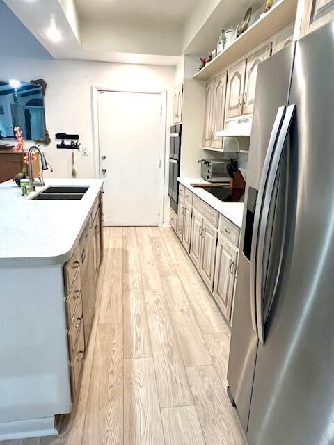6582 Patio Ln, Boca Raton, FL 33433 - kitchen featuring black appliances, a sink, light wood-type flooring, under cabinet range hood, and light countertops