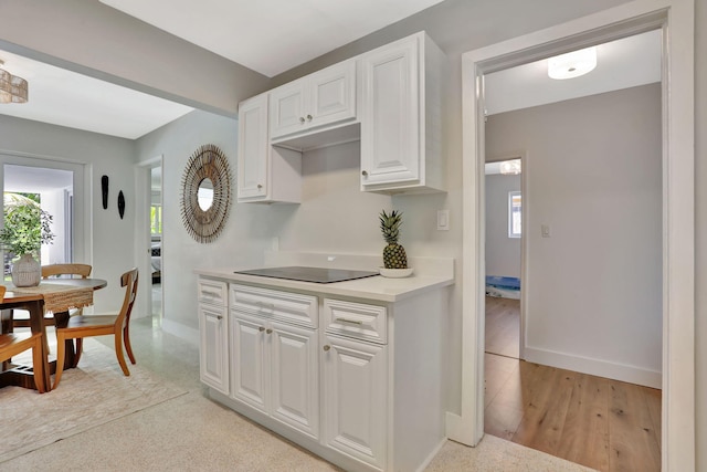kitchen featuring plenty of natural light, black electric stovetop, white cabinets, and baseboards