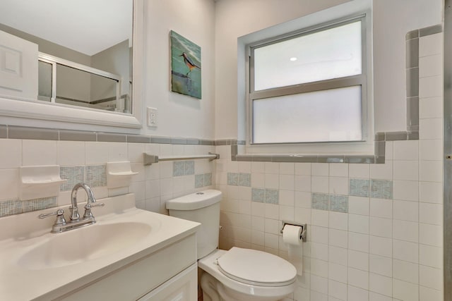 full bathroom featuring a shower stall, toilet, vanity, wainscoting, and tile walls