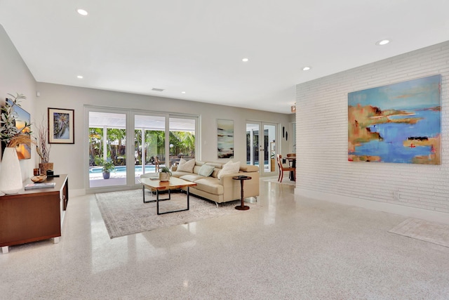 living room featuring french doors, dark speckled floor, recessed lighting, brick wall, and baseboards