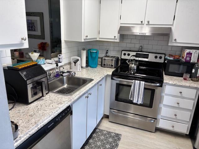 kitchen with tasteful backsplash, white cabinets, appliances with stainless steel finishes, under cabinet range hood, and a sink