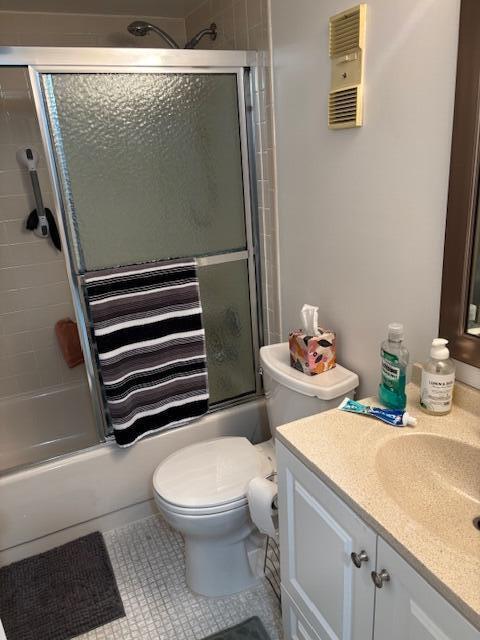 full bath featuring combined bath / shower with glass door, tile patterned flooring, vanity, and toilet