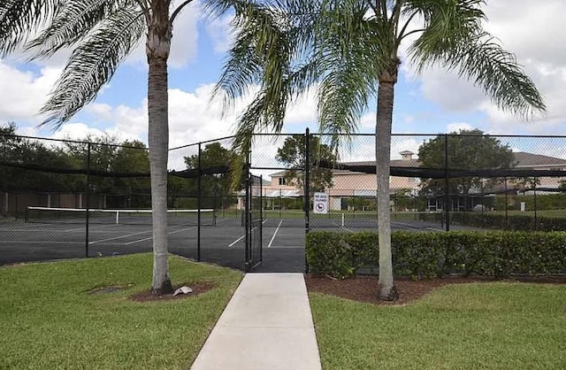 exterior space featuring a tennis court, fence, and a lawn