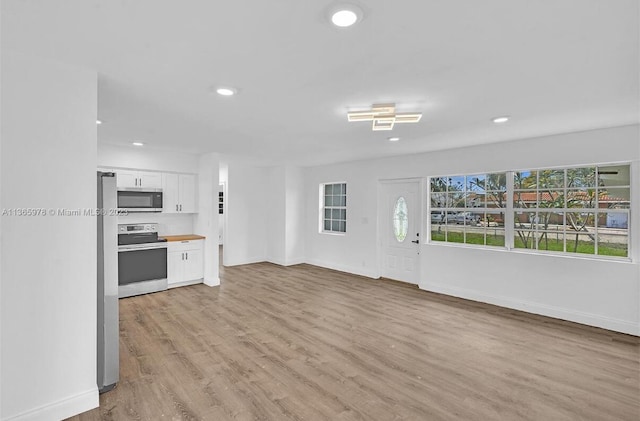 interior space with baseboards, recessed lighting, white cabinets, stainless steel appliances, and light wood finished floors