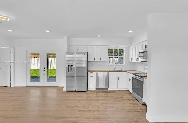 kitchen with french doors, white cabinetry, appliances with stainless steel finishes, light wood finished floors, and a sink