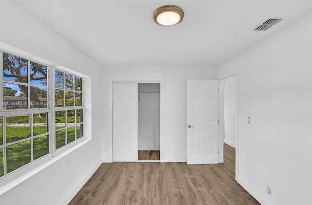 unfurnished bedroom with wood finished floors, baseboards, a closet, and visible vents