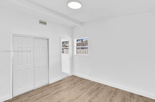 unfurnished bedroom featuring visible vents, baseboards, a closet, beamed ceiling, and wood finished floors
