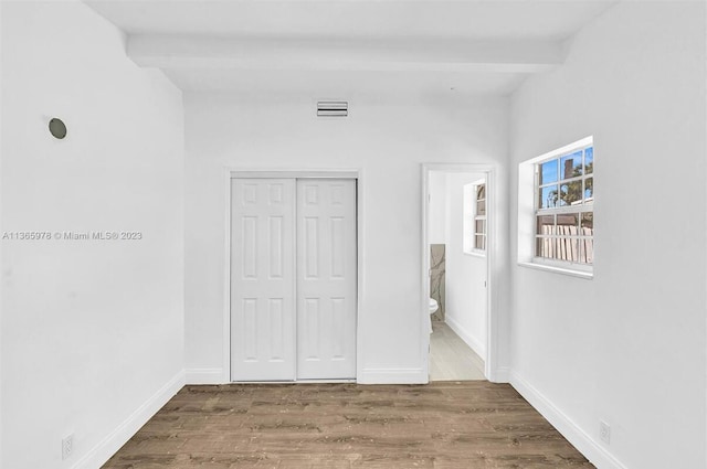 unfurnished bedroom featuring beamed ceiling, baseboards, wood finished floors, and visible vents