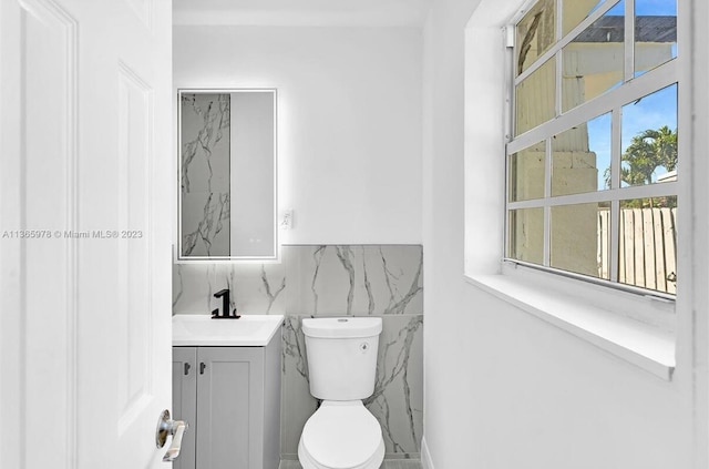 half bathroom featuring toilet, vanity, and tile walls