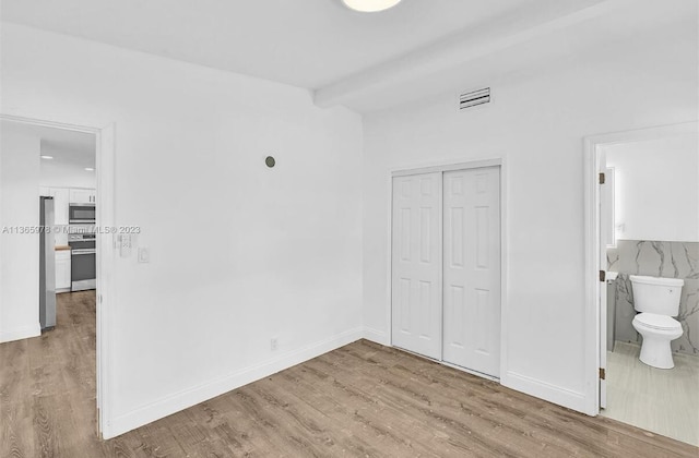 unfurnished bedroom featuring visible vents, a closet, freestanding refrigerator, and wood finished floors