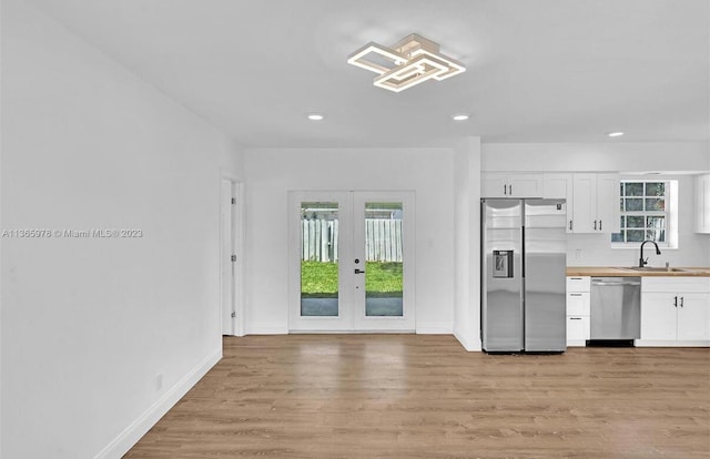 kitchen with light wood-type flooring, white cabinetry, appliances with stainless steel finishes, a sink, and french doors