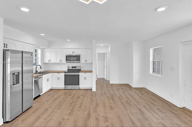 kitchen with light wood-type flooring, appliances with stainless steel finishes, a sink, and white cabinetry