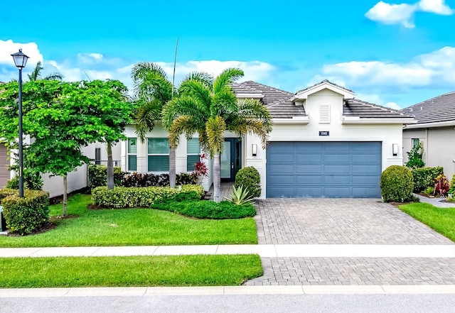 ranch-style house featuring a front yard, a garage, a tile roof, stucco siding, and decorative driveway