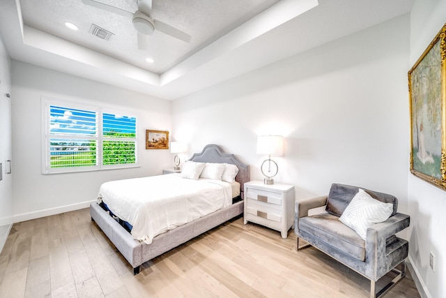 bedroom featuring a tray ceiling, light wood-type flooring, baseboards, and visible vents