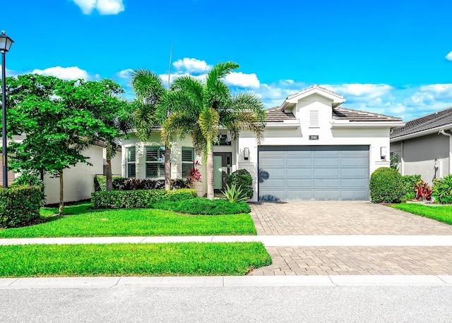 view of front of house with a tiled roof, stucco siding, decorative driveway, a front yard, and an attached garage