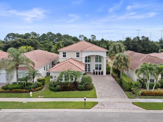 mediterranean / spanish home with stucco siding, a tile roof, a front lawn, and decorative driveway
