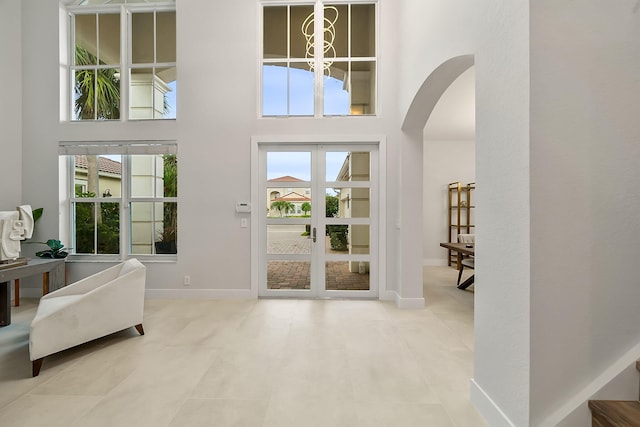 entrance foyer with arched walkways, a high ceiling, baseboards, and a healthy amount of sunlight
