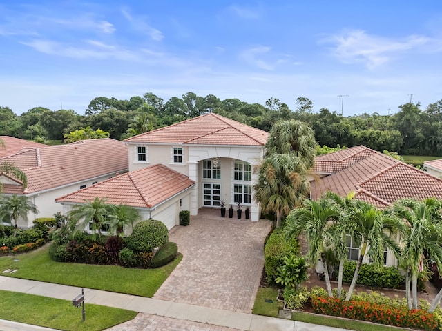 mediterranean / spanish-style home featuring driveway, a tiled roof, french doors, a front lawn, and a garage