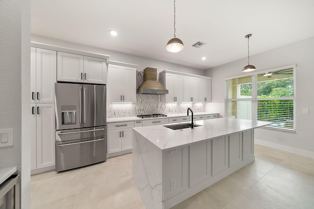 kitchen featuring wall chimney exhaust hood, a sink, tasteful backsplash, an island with sink, and appliances with stainless steel finishes