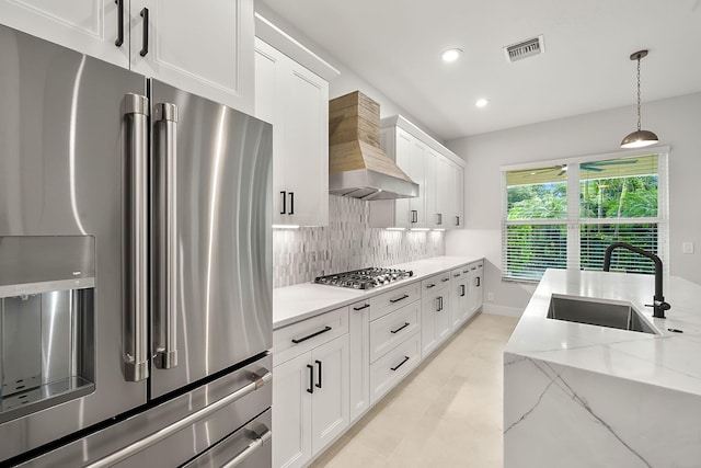 kitchen featuring white cabinets, a sink, backsplash, wall chimney range hood, and appliances with stainless steel finishes