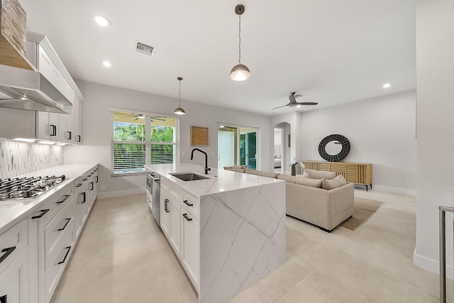 kitchen with wall chimney exhaust hood, a ceiling fan, a sink, and stainless steel gas stovetop