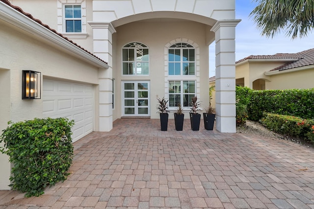view of exterior entry with stucco siding, decorative driveway, and a garage