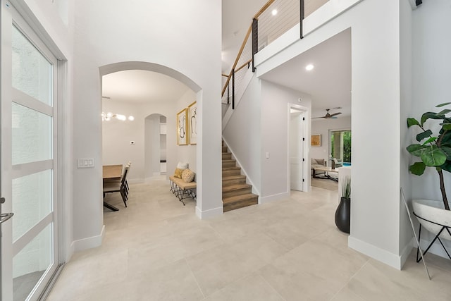 tiled entryway featuring stairway, a high ceiling, a ceiling fan, arched walkways, and baseboards