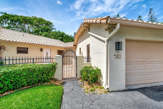 view of home's exterior with an attached garage, stucco siding, fence, and a gate