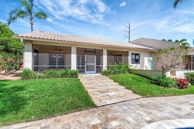 view of front facade featuring a tiled roof, ceiling fan, a front lawn, and stucco siding